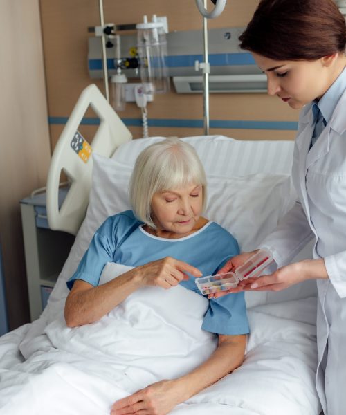 female doctor giving pills to senior woman lying in hospital bed