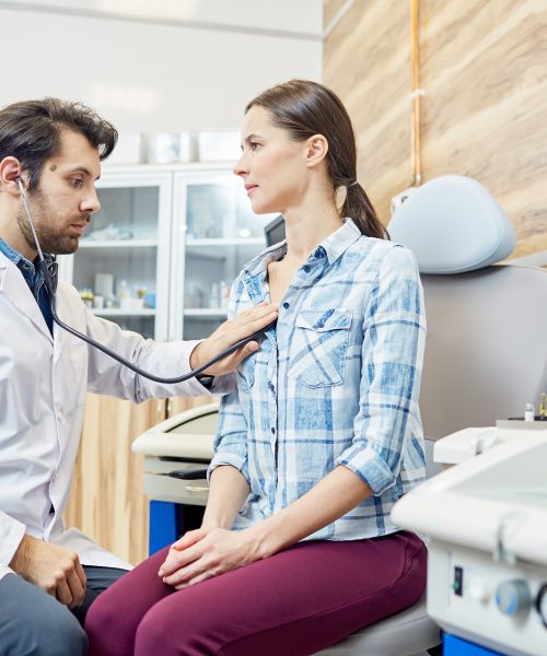 Therapeutist with stethoscope listening to lungs of his young patient during appointment